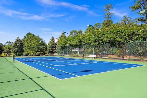 A tennis court surrounded by trees and a fence.