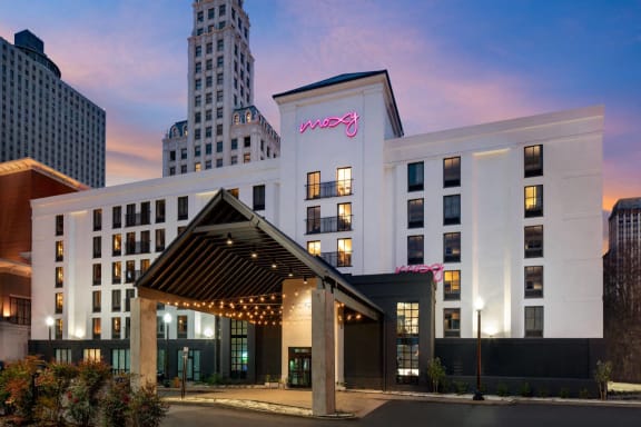 a white hotel building with a pink neon sign on the side of it