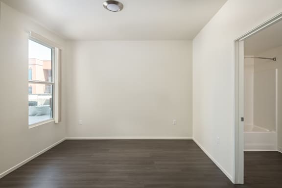 a bedroom with white walls and wood flooring and a window