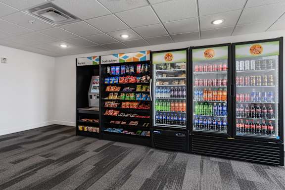 Self-service snack station with a 'Pay Here' kiosk, chips, and assorted bottled sodas and water. 605 Place Student Housing & Co-Living, St George, 84770