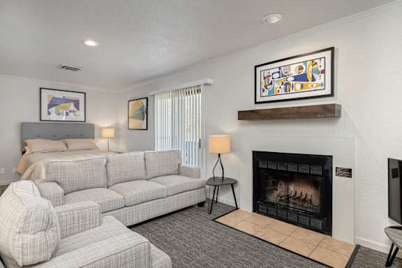 A living room with a grey couch, a fireplace, and a painting on the wall.