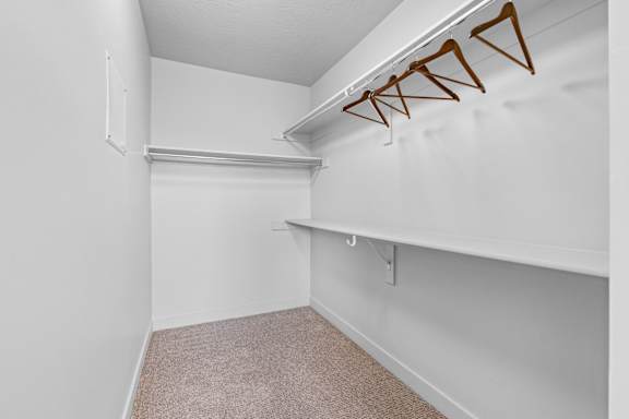 A white closet with a carpeted floor and a white shelf.