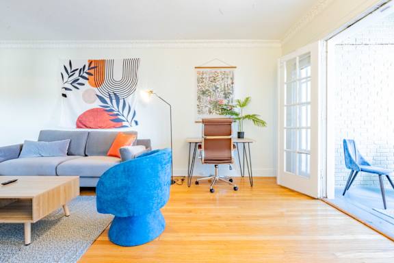 A blue chair sits in a room with a grey couch and a wooden table.