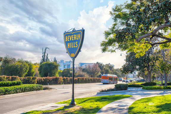 A sign that says Beverly Hills stands in the middle of a street.