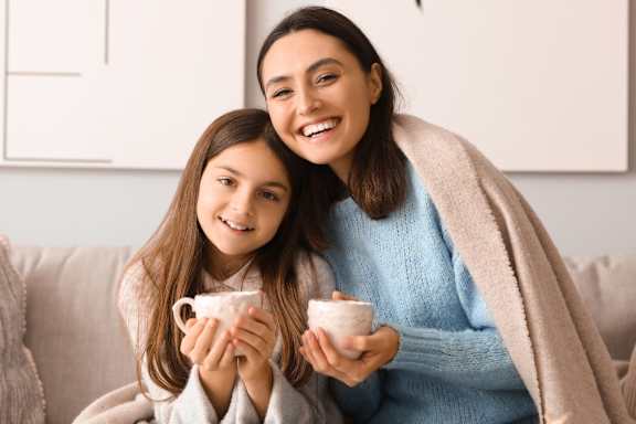 A woman and a girl are sitting on a couch, both wearing bathrobes and holding cups.