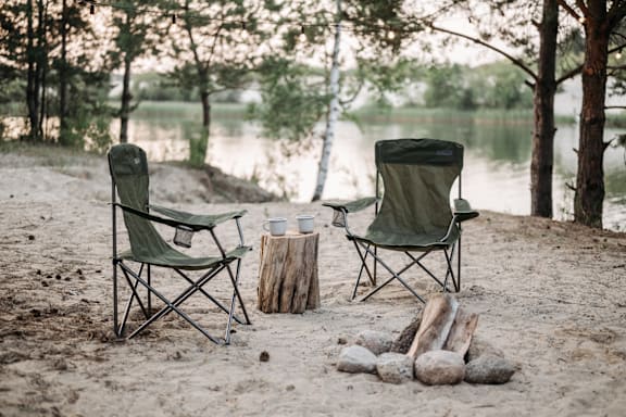 a couple of camping chairs sitting on the sand next to a lake