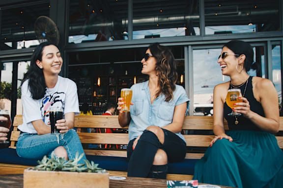 three women sitting on a bench drinking beer