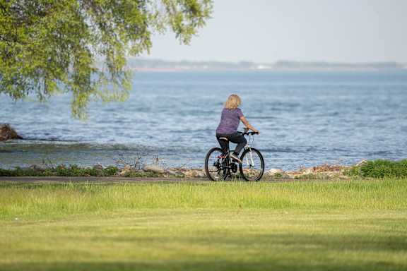A person riding a bicycle on a grassy area near a body of water.