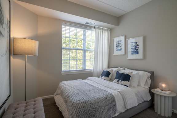 A bedroom with a large bed and a window with blinds.