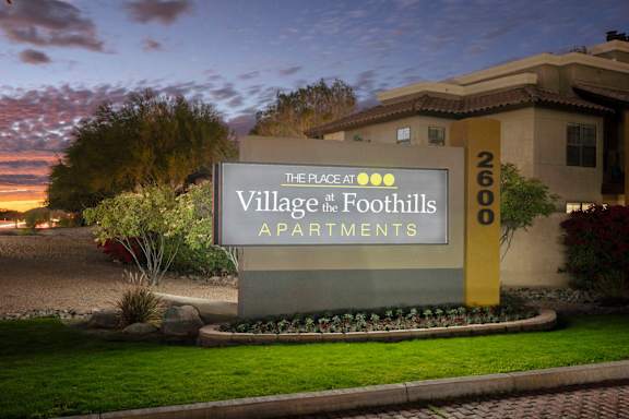 A sign for the Village at the Foothills Apartments is displayed in front of a building.