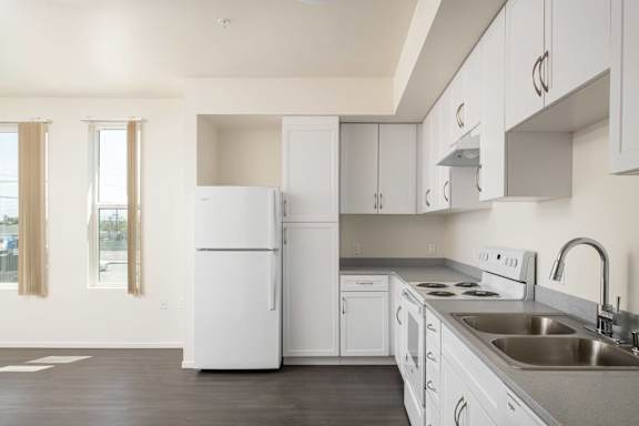 A white refrigerator is in a kitchen with white cabinets and a stainless steel sink.