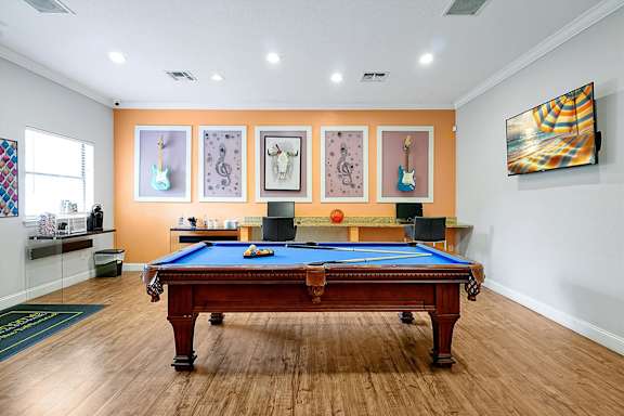 A pool table in a room with orange walls and a painting on the wall.