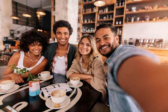 Four people are sitting at a table with cups of coffee in front of them.