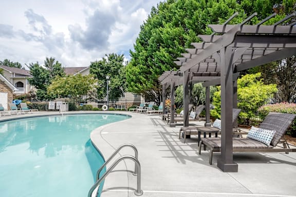 A pool with a metal ladder and a pergola with cushioned seating.