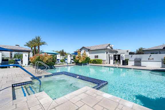 A swimming pool surrounded by a tiled patio and a building in the background.
