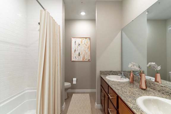 A bathroom with a sink, mirror, toilet, and a painting hanging on the wall.