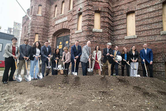 A group of people holding shovels in front of a brick building.