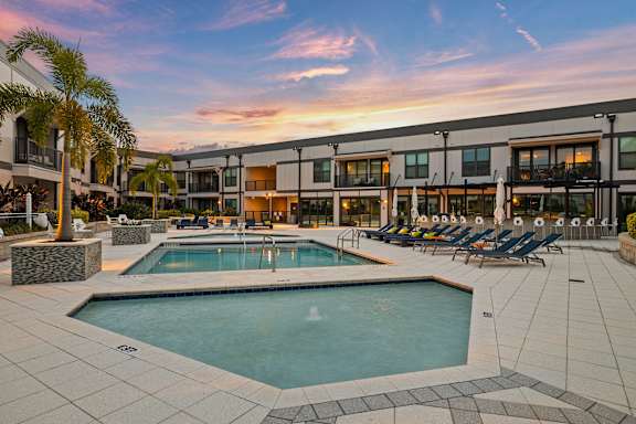 a swimming pool with chairs around it in front of a building