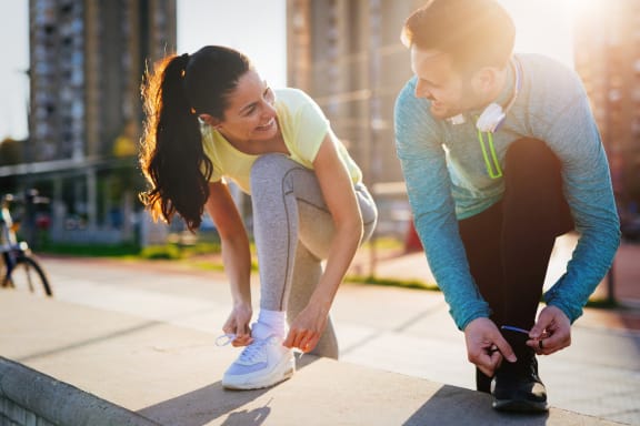 Couple in Athletic Clothing Tying Shoes on Side of Cement Wall While Looking at Each Other and Smiling