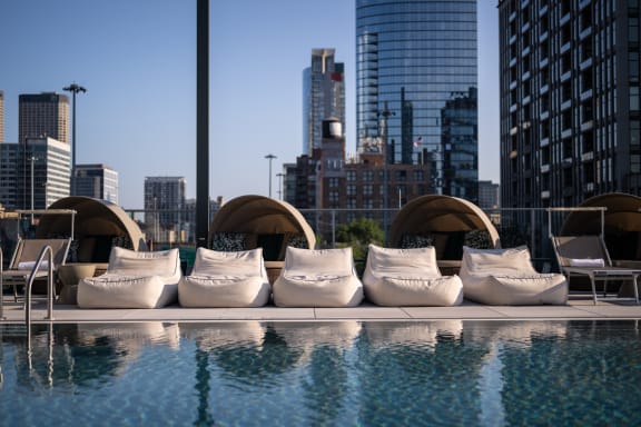 an outdoor pool with white lounge chairs and a city skyline in the background