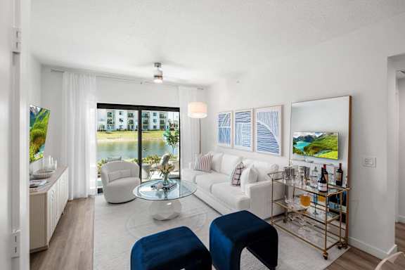 A living room with a white couch, a blue ottoman, and a glass coffee table