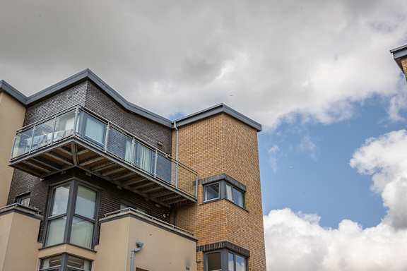 the side of a brick building with a balcony and a cloudy sky