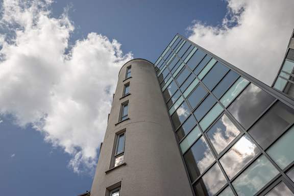 the side of a tall building with clouds reflected in the windows