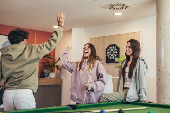 three women laughing and playing pool in a living room
