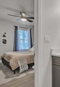 A bathroom with a vanity, mirror, and a bedroom with a bed and a window.