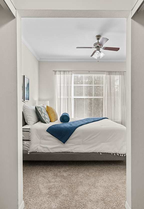 A bedroom with a bed, a ceiling fan, and a window with blinds.