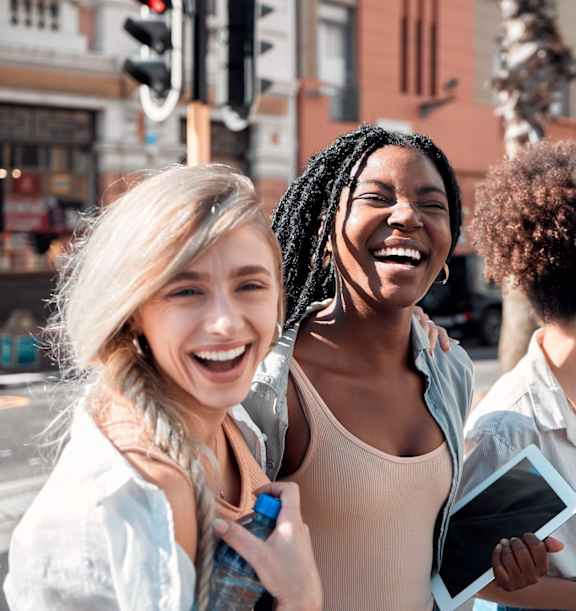 Four people are standing on a street corner, laughing and looking at a tablet.