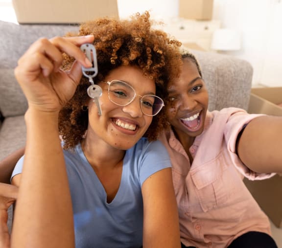 two young women sitting on a couch holding up a remote control