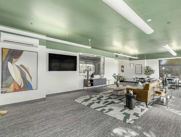 A modern living room with a grey carpet and a painting on the wall.
