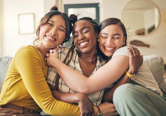 Three women hugging each other in a living room.