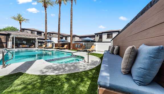 A pool surrounded by palm trees and a wooden bench.