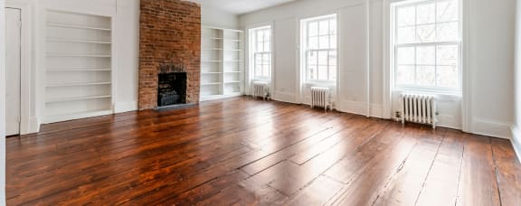 an empty living room with hardwood floors and a brick fireplace