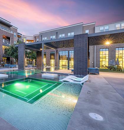 a pool area with a hot tub and chaise lounge chairs in front of an apartment building