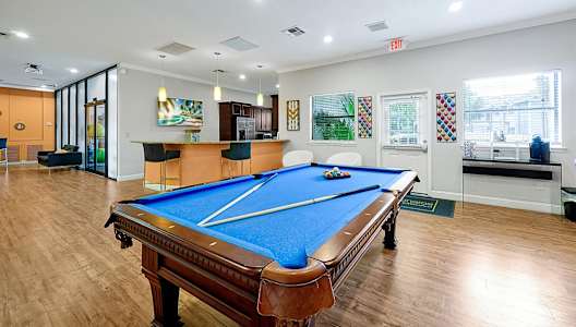 A pool table is in the middle of a room with a bar and a painting on the wall.
