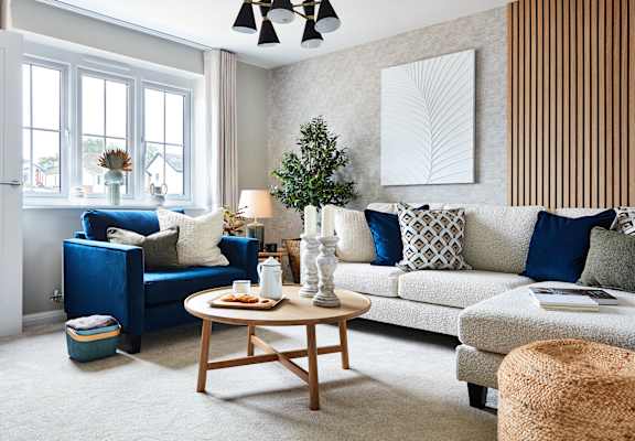 A living room with a white couch, blue ottoman, and a wooden coffee table.