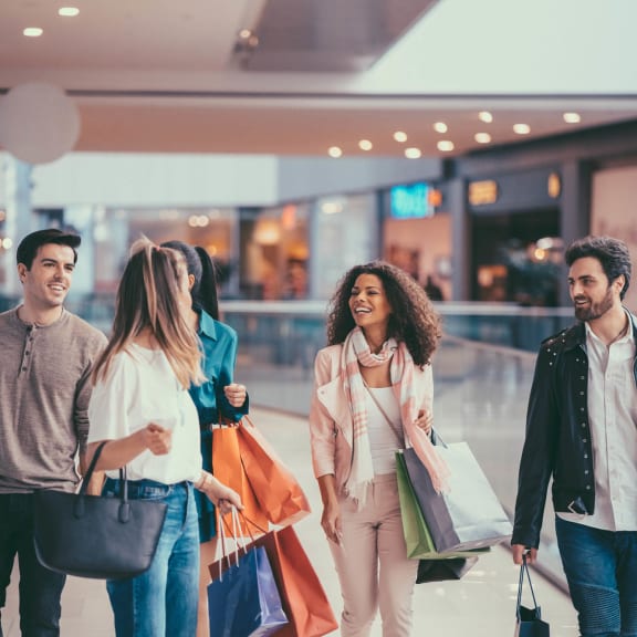 A group of stylish young adults is enjoying a shopping trip in a modern mall, carrying multiple colorful shopping bags and chatting happily.