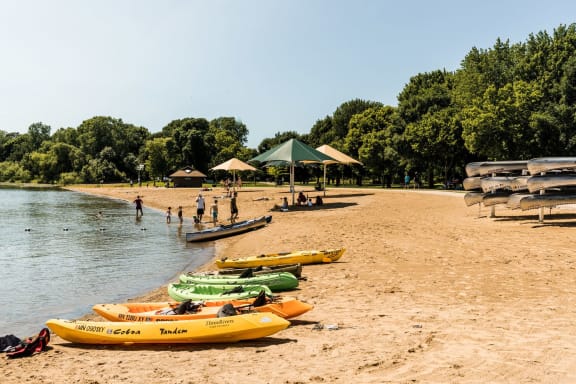a beach at the lake with kayaks and people on the sand