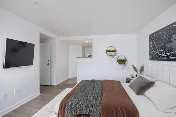 A bedroom with a bed, a flat screen TV, and a white wall with a black and white drawing.