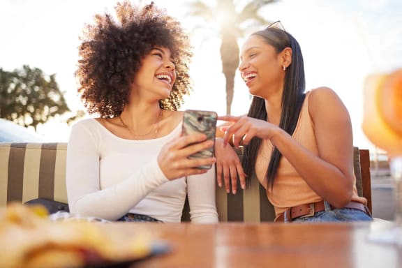 two women sitting on a couch laughing and looking at a cell phone