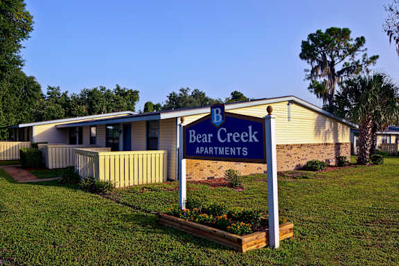Bear Creek Apartments is a residential complex with a well-maintained lawn and a clear blue sky.