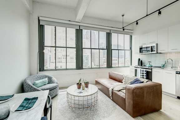 A modern living room with a brown leather couch, a grey armchair, and a white coffee table.