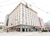 Thumbnail 8 of 8 - A large, old building with many windows sits in the middle of a city street.