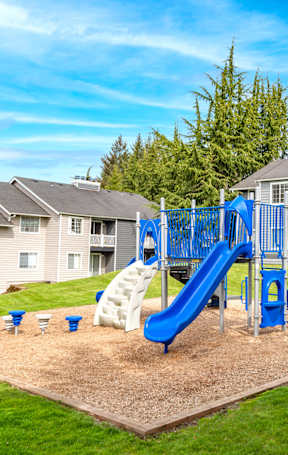 A playground with a blue slide and white slide in the middle of a sandy area.