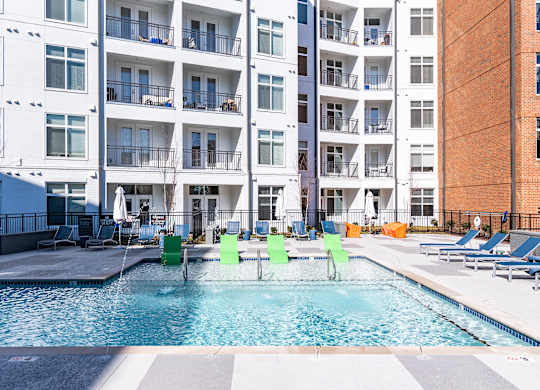 a swimming pool with green chairs in front of an apartment building