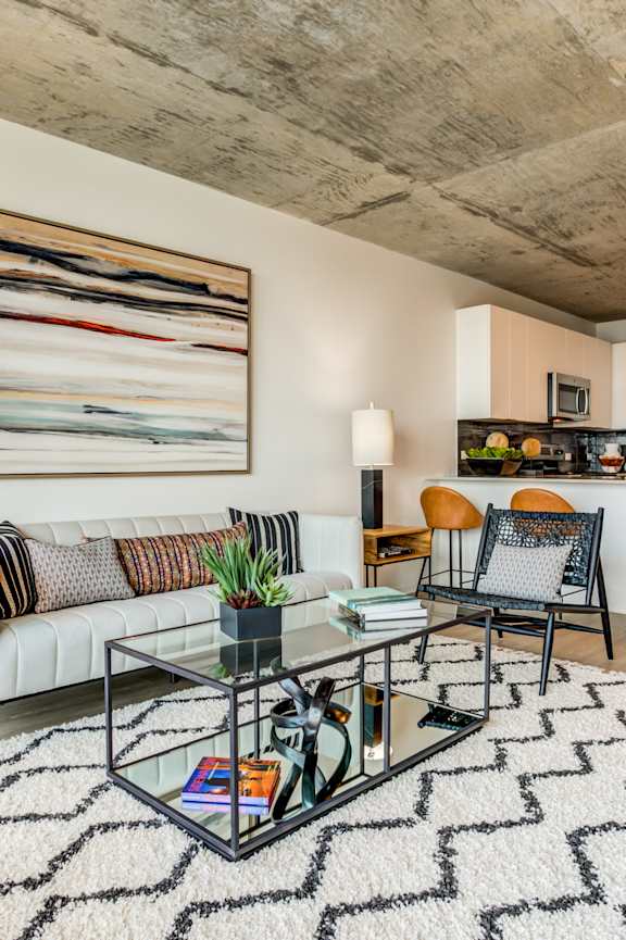 A modern living room with a glass coffee table and a large abstract painting on the wall.