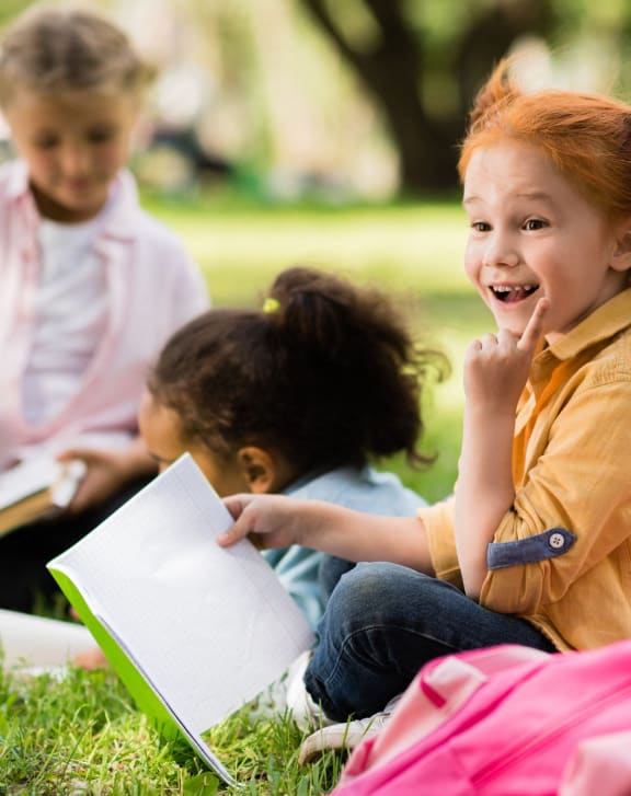 a group of children sitting in the grass reading books